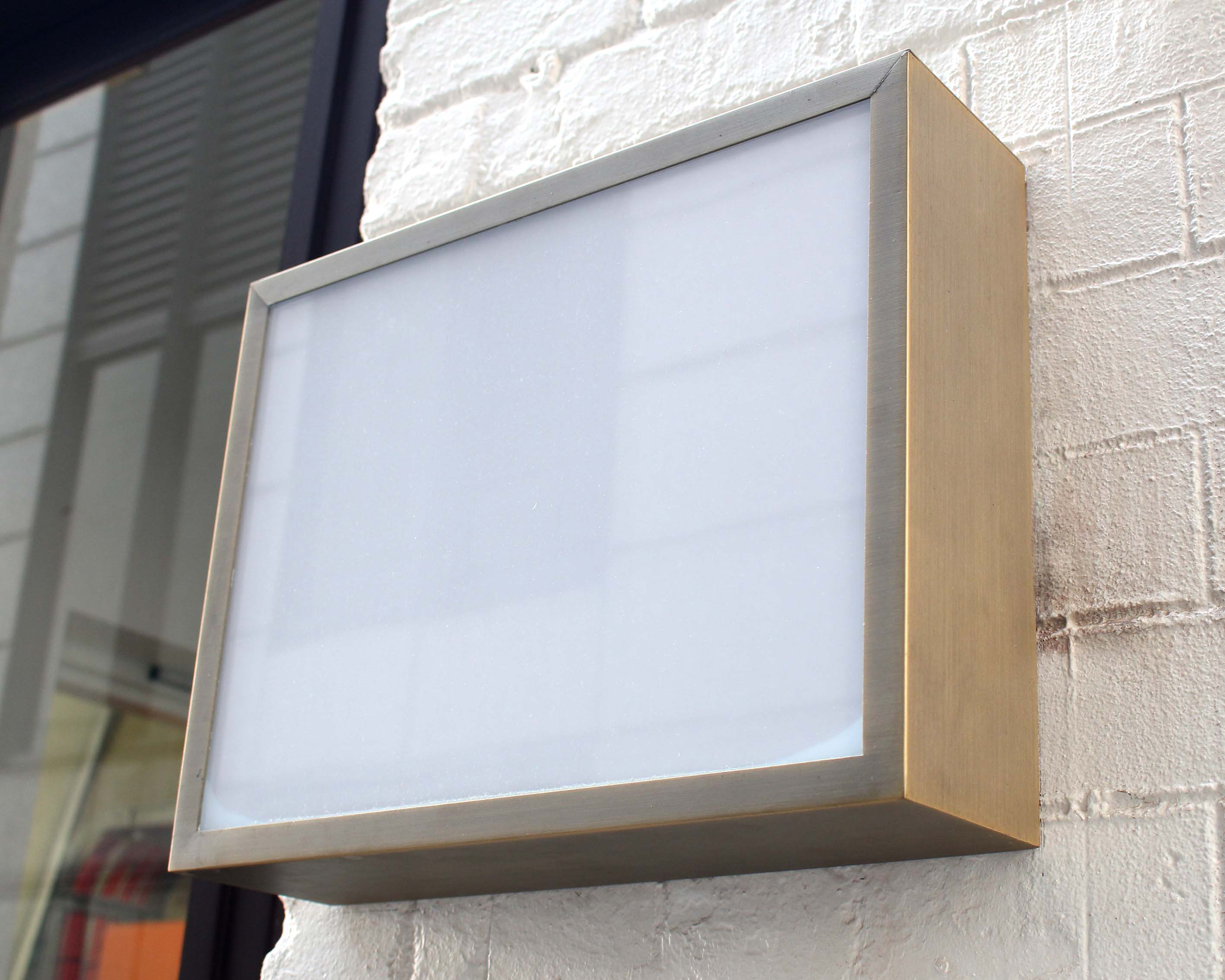 An external signage illuminated lightbox with a stainless steel frame attached to a wall.