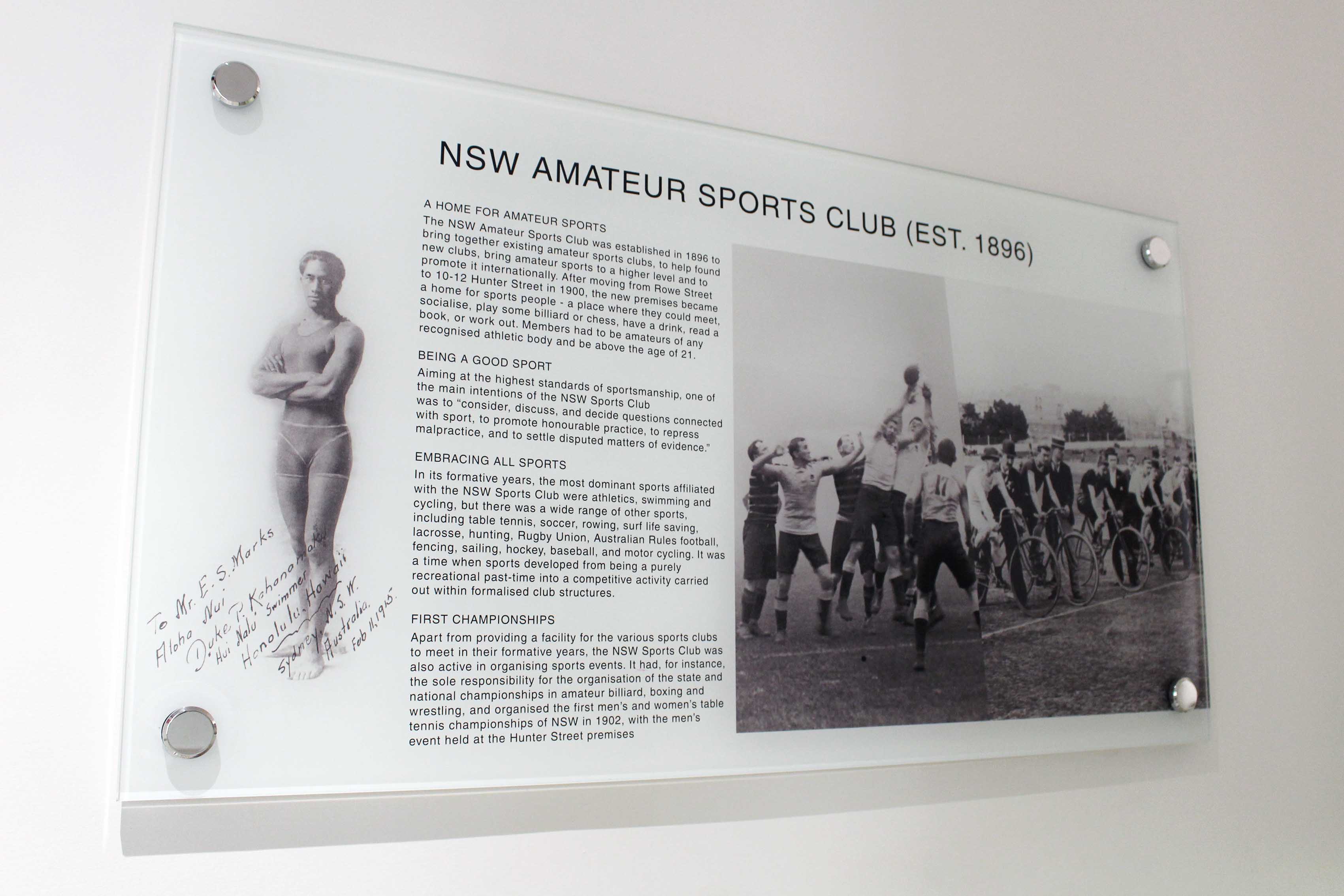 Pin mounted glass informational and pictorial black and white display of the NSW Amateur Sports Club.