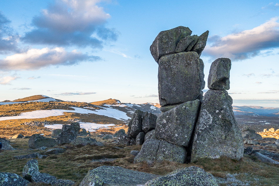 Photo of a mountain scape with snow and large rock boulders in foreground
