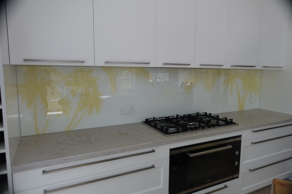 A kitchen with a custom glass printed splashback of yellow palm trees on a white background