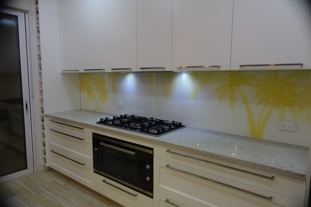 A kitchen with a custom glass printed splashback of yellow palm trees on a white background
